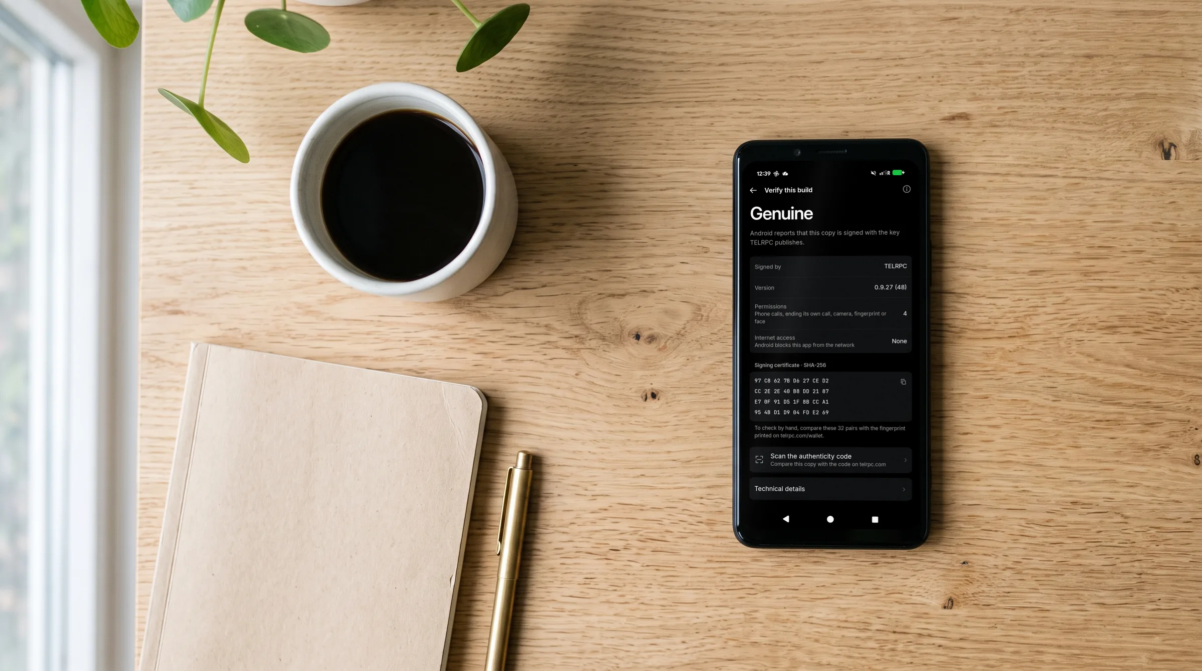 A phone lying on an oak desk beside a coffee cup and a notebook, showing the TELRPC Wallet's Verify this build screen: signed by TELRPC, with its permission list